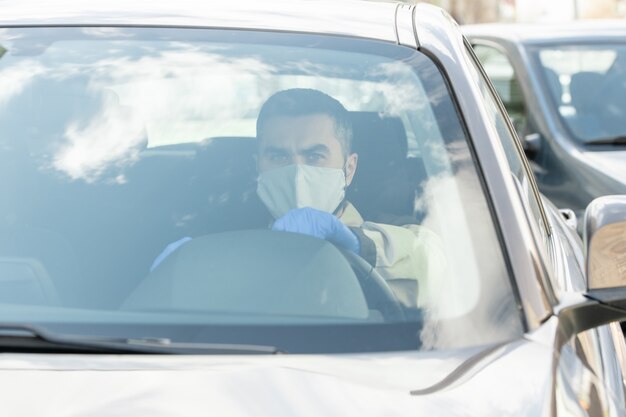 Contemporary courier in mask and gloves driving to clients while delivering online shop orders or food products from supermarket