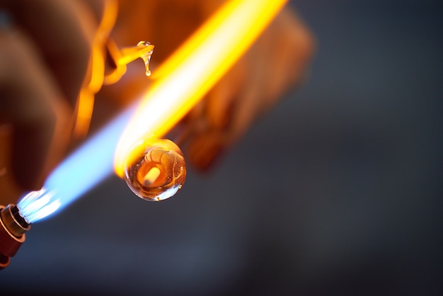 Artigiano creativo contemporaneo che brucia il pezzo di vetro mentre lo si tiene vicino al fuoco che esce dal bruciatore durante la lavorazione a lume