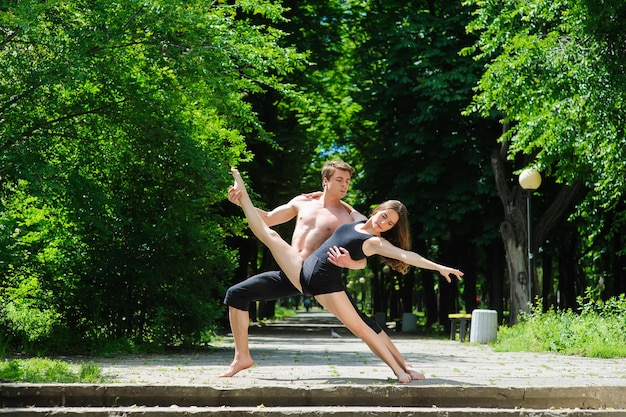 Contemporary dance Man and woman in passionate dance pose in park Young couple dancing modern dance Girl doing splits Man with naked torso Old park trees in background