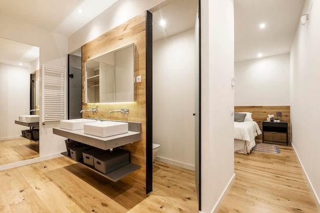 貸別荘の脱衣所にある、フレームレスの鏡が付いた自立型シンクが 2 つある現代的な装飾のトイレ
