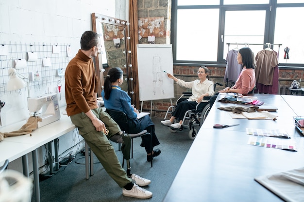 Contemporary designers looking at whiteboard while their colleague making presentation