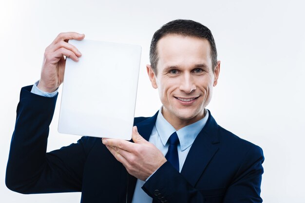 Photo contemporary device. happy smart pleasant businessman smiling and holding up a tablet while showing it to you