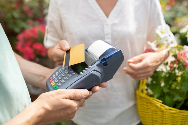 Acquirente femminile contemporaneo che utilizza la carta di credito per pagare alcuni fiori freschi in vaso in un garden center contemporaneo