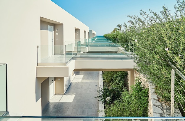 Contemporary hotel building large empty terraces with glass railings near green trees at resort