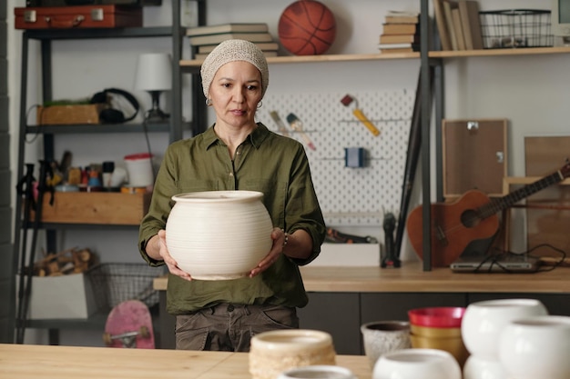 Contemporary retired female carrying large white clay vase or\
flowerpot