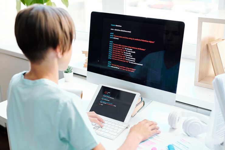 Photo contemporary schoolboy sitting by desk in front of computer monitor while analyzing data or preparing report for seminar