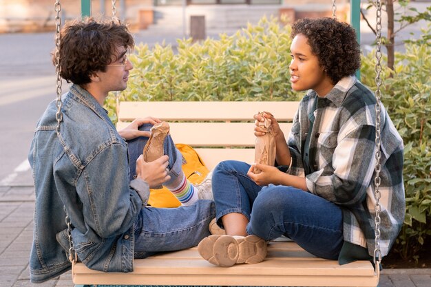 Foto coppia di adolescenti contemporanei con bevande che discutono di piani