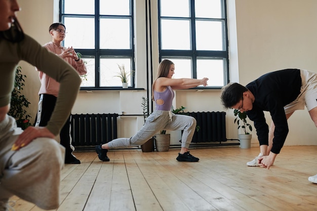 Contemporary teenagers doing stretching exercises on wooden floor of studio