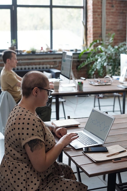 Contemporary young businesswoman sitting by table in front of laptop