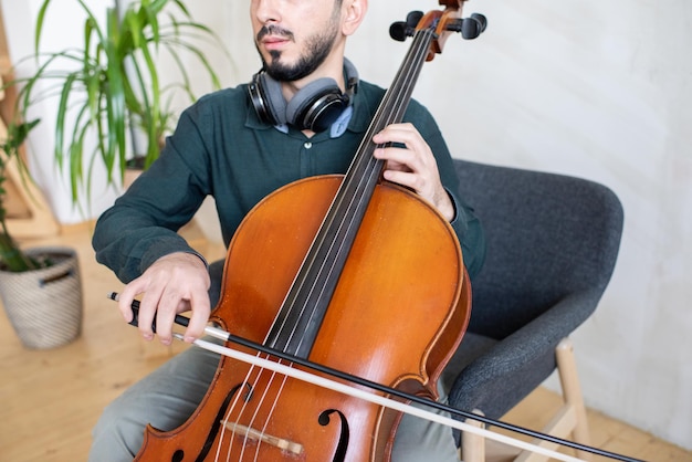 Contemporary young man gliding fiddlestick against strings of cello