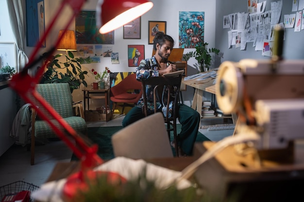 Contemporary young man sitting in studio of arts or workshop and drawing