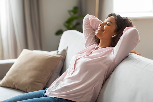 Content black woman using earphones on sofa in living room