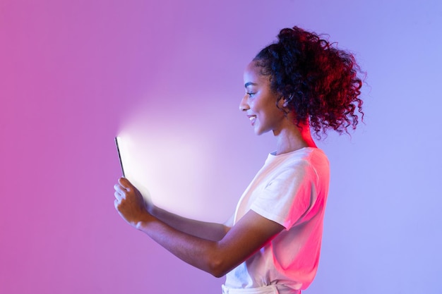 Content black woman with tablet glowing on purplepink background