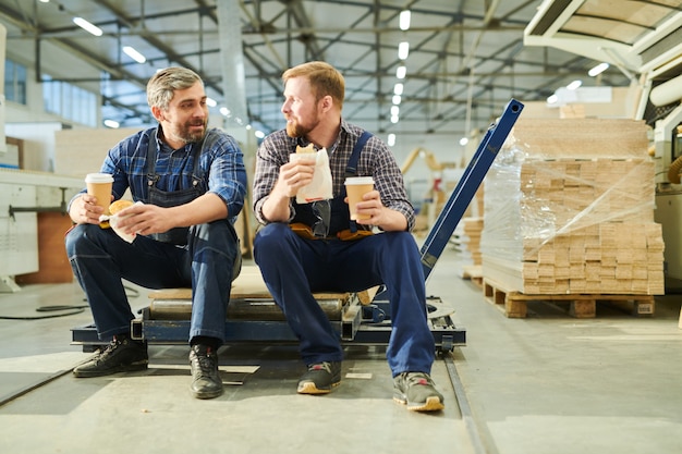 Content colleagues in workwear drinking coffee in factory shop