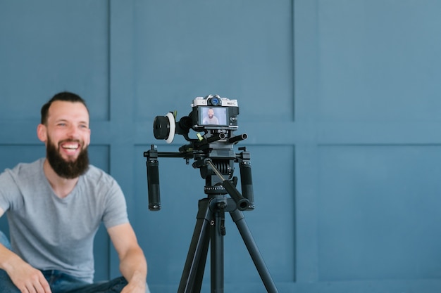 Content creation for social media. blogger shooting video of himself using camera on tripod. smiling bearded hipster man