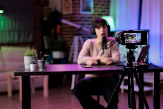 Content creator vlogging lifestyle podcast episode on camera, using live broadcasting equipment in studio. Female vlogger recording online talk show conversation, web livestream.