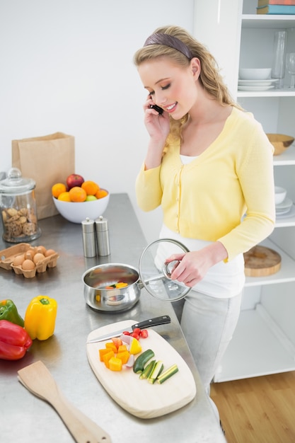 Content cute blonde phoning while preparing a meal