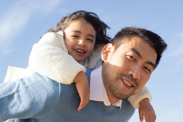 Content Japanese family spending time on beach. Father and daughter playing, smiling, riding on back, fooling around. Leisure, family time, parenting concept