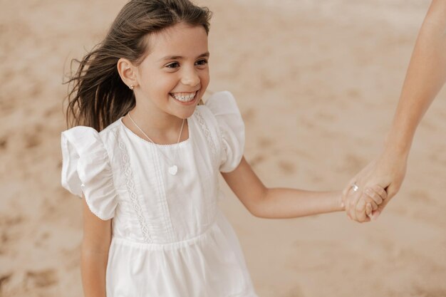 Content kid smiling while holding hand of crop mom on sandy seashore