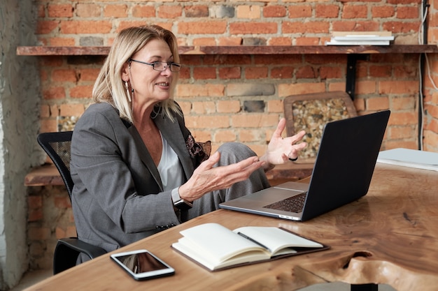 Content mature lady inspired with own ides presenting her plan while videoconferencing with business partner using laptop