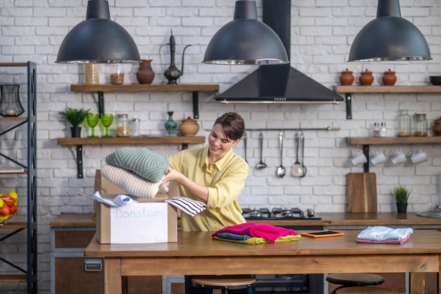 Contented Caucasian woman putting items of clothing into the carton