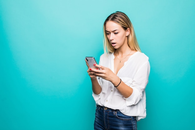 Contented smiling woman typing text message or scrolling through social networks using smartphone isolated over blue wall