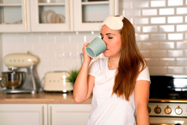 Foto donna dolce contenta che beve caffè nella sua cucina a casa femmina carina che tiene una tazza di buongiorno