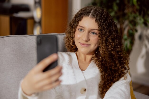 満足している女性は彼女の手で彼女の携帯電話を保持しているリビングルームのソファに座っています