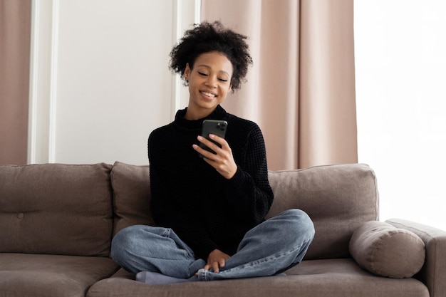 A contented young woman using the phone is sitting on the sofa at home Uses the app online shopping