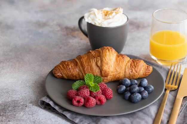 Continentaal ontbijt, Franse croissant, koffie met melk, bessen en sinaasappelsap.