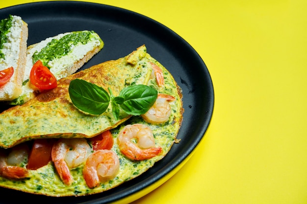 Continentaal ontbijt - omelet met garnalen, tomaten en basilicum met toast met roomkaas en pesto op een zwarte plaat op s.