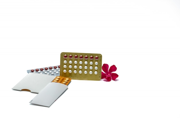 Противозачаточные таблетки или противозачаточные таблетки с розовым цветком на белом фоне с копией пространства. Гормон для контрацепции. Концепция планирования семьи. Белые и красные круглые гормональные таблетки в блистерной упаковке