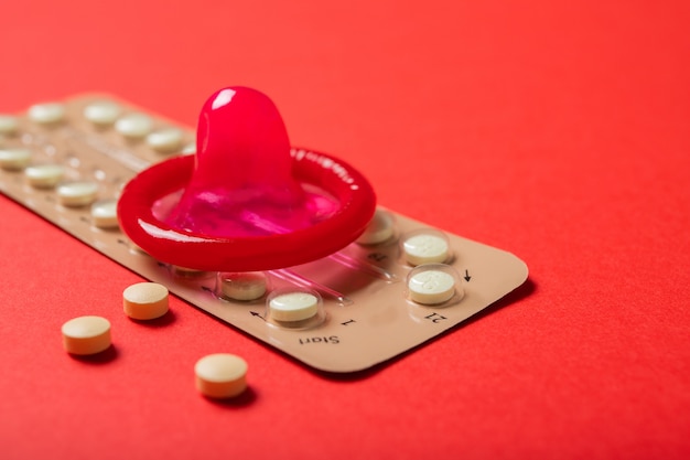 Contraceptive pills and a condom on a red background