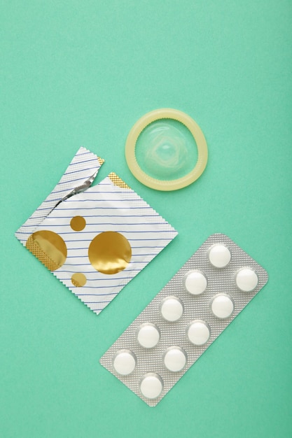 Contraceptive pills and condoms on mint background Concept of birth control