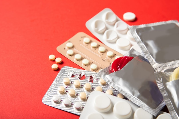 Contraceptive pills and condoms on a red background