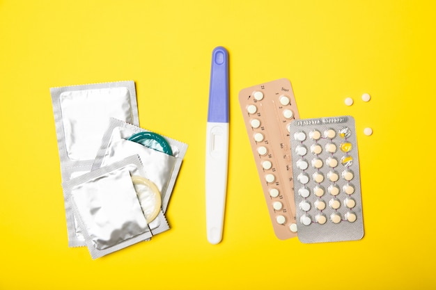 Contraceptive pills and condoms on a yellow background