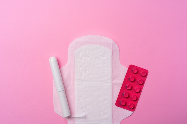 contraceptive pills, hygienic pads and tampons on pink top view