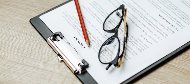 A contract on a wooden work table with glasses and a red pencil. The documents are ready for signing. Business concept. Collaboration agreement.