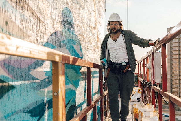 Contractor, artist at high altitude in a building cradle performs facade painting