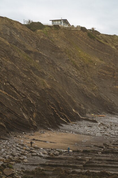 Photo contrast between a cliff with a house on the edge and people on the beach.