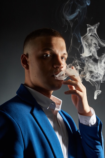 Foto ritratto di contrasto di un uomo d'affari uomo di fumo in un completo costoso su sfondo scuro.