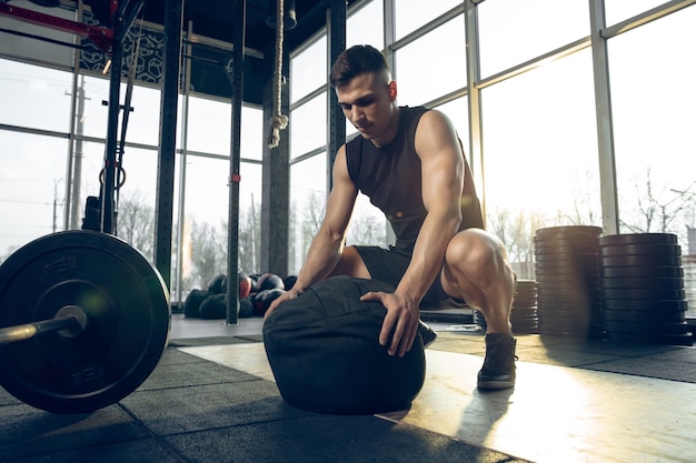 Control. Young muscular caucasian athlete training in gym, doing strength exercises, practicing, work on his upper body with weights and ball. Fitness, wellness, sport, healthy lifestyle concept.