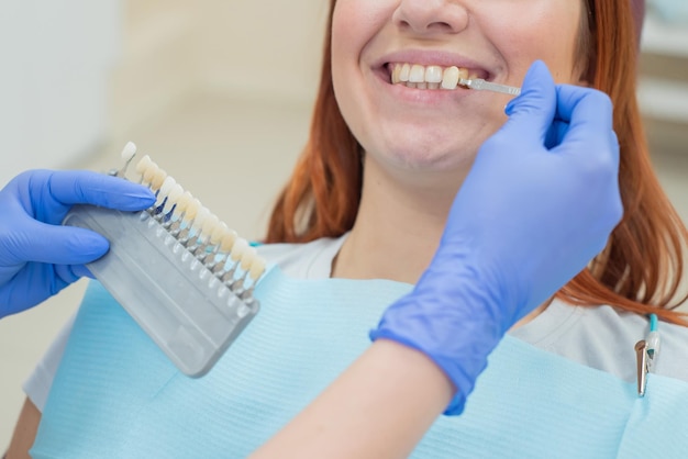 Controleer en selecteer de kleur van de tanden in de tandartsstoel Tandarts maakt het proces van de behandeling van een mooi jong roodharig meisje Selectie van een tandimplantaat Close-up