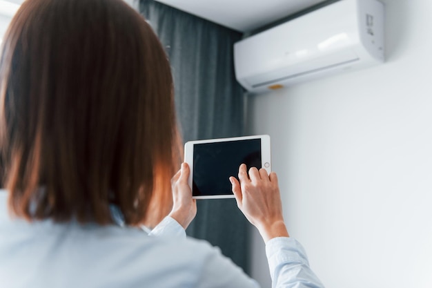 Controlling conditioner by tablet Young woman is indoors in room of modern house at daytime