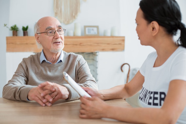 Controversial book. Volunteer holding book while communicating with attractive pleasant senior man and staring at him