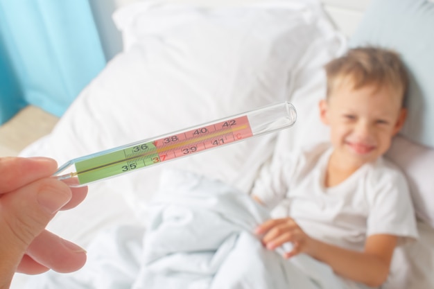 회복기. 수은 온도계는 아기의 정상적인 체온을 나타냅니다. 감기와 독감에서 회복하는 어린 소년.