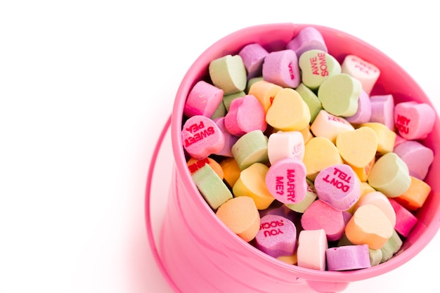 Conversation heart candies in pink bucket.