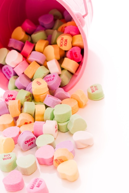 Conversation heart candies spilled from pink bucket.