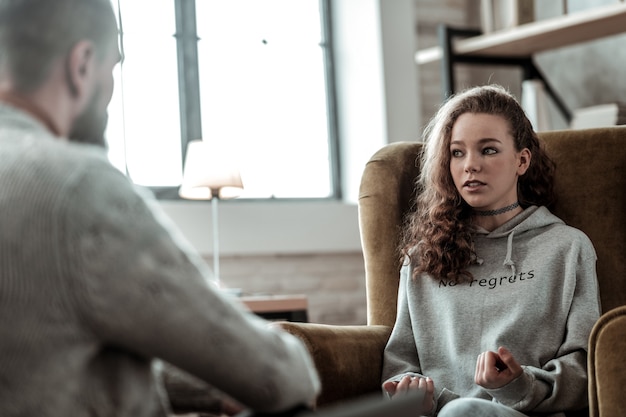 Conversation with psychologist. Appealing teenage girl feeling involved in conversation with psychologist