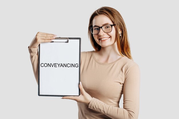 Conveyancing. Beautiful young business woman wearing glasses holds a clipboard with mock up space isolated on gray background
